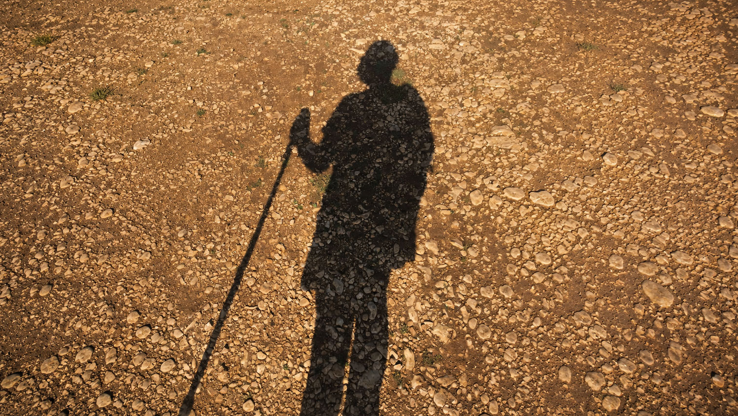 Sombra de un peregrino con mochila y bastón caminando por el Camino de Santiago